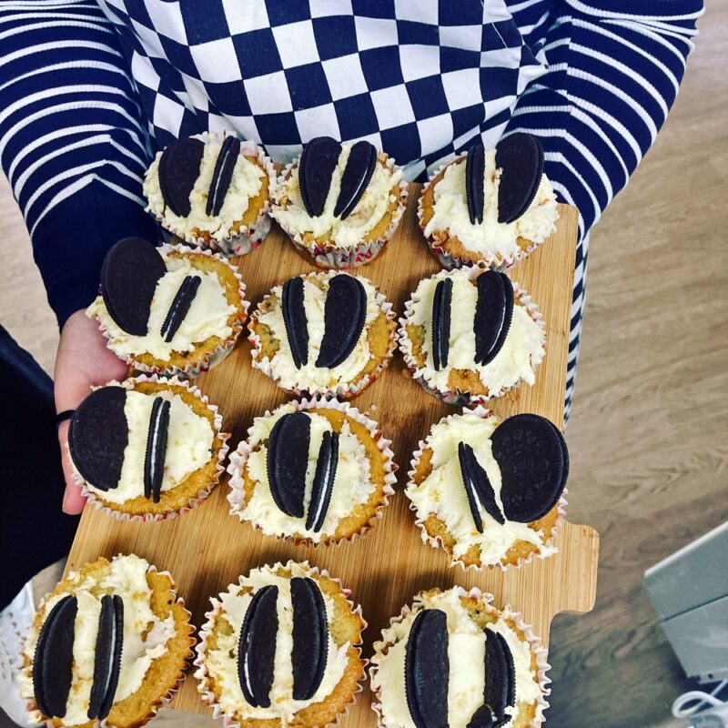 A person is holding a tray of 12 butterfly wing muffins, You can only see their body and arms.  