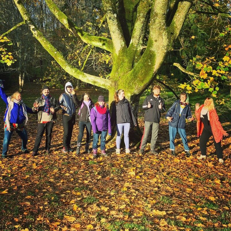 A group of young people standing in fornt of a large tree in autumn. 