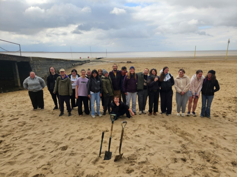 A group of 20 young people on the beach looking at the camera