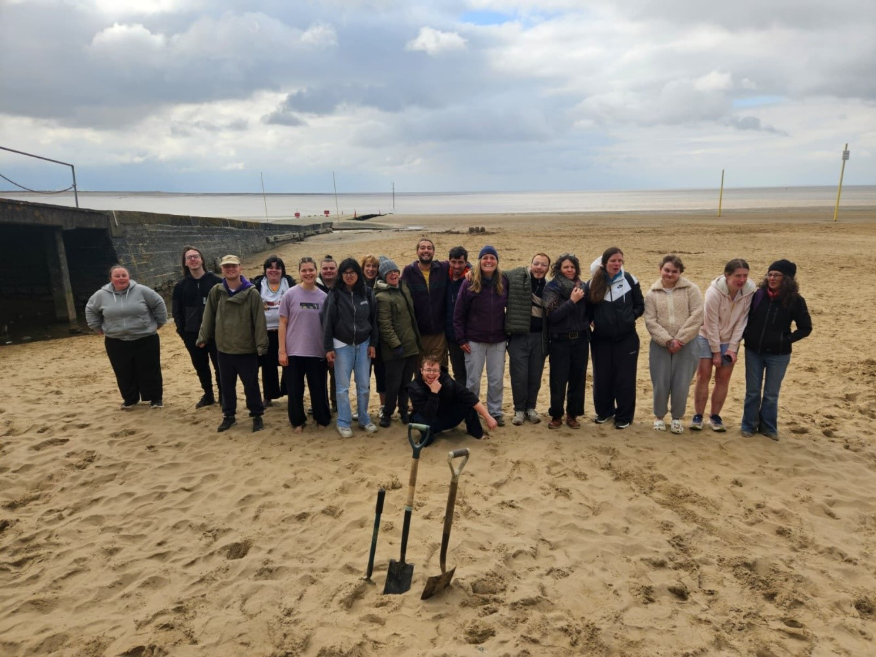 A group of 20 young people on the beach looking at the camera